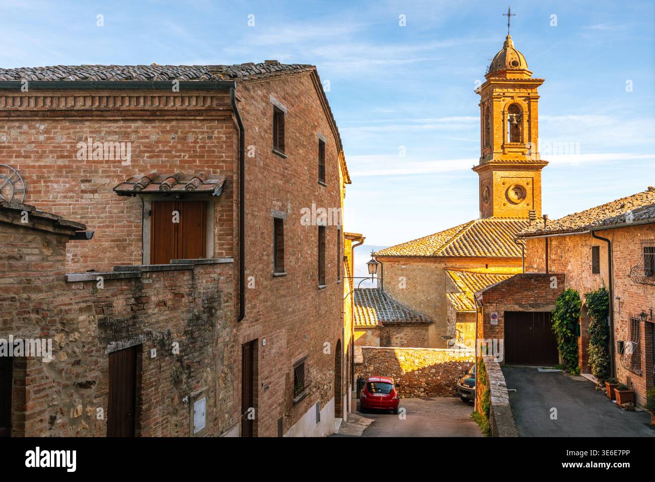 Montepulciano, Italien - 8. November 2022: Historische Backsteinbauten säumen eine enge Straße mit einem markanten Kirchturm. Stockfoto