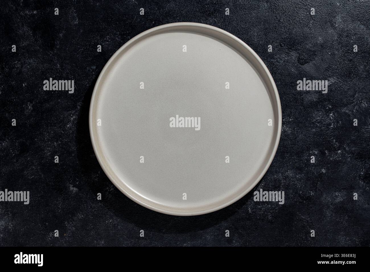 Minimalistischer Draufsicht auf leere Keramikplatte auf dunkler strukturierter Oberfläche mit Kopierraum, ideal für die Präsentation von Speisen, das Design von Restaurants und Mo Stockfoto