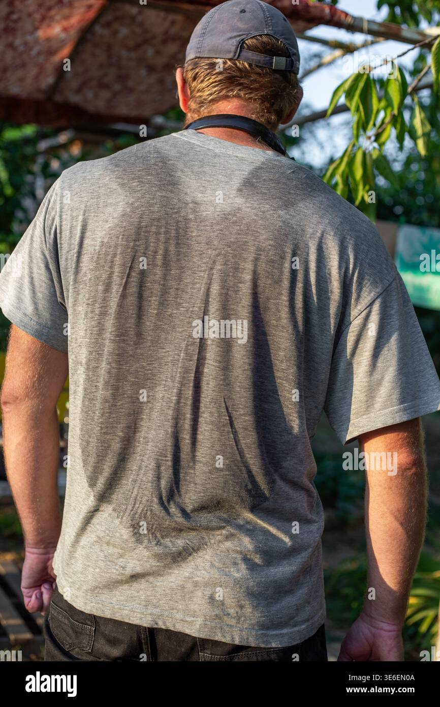 Der Mann trägt ein graues T-Shirt und schwarze Shorts, steht draußen mit Bäumen hinter ihm. Sommertag, Freizeitkleidung, draußen. Stockfoto