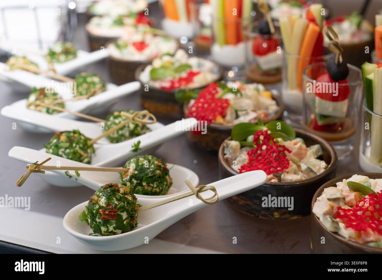 Gourmet-Vorspeisen mit Kräuterkäsebällchen auf Löffeln und russischen Salatschüsseln am Bankettbuffet. Stockfoto