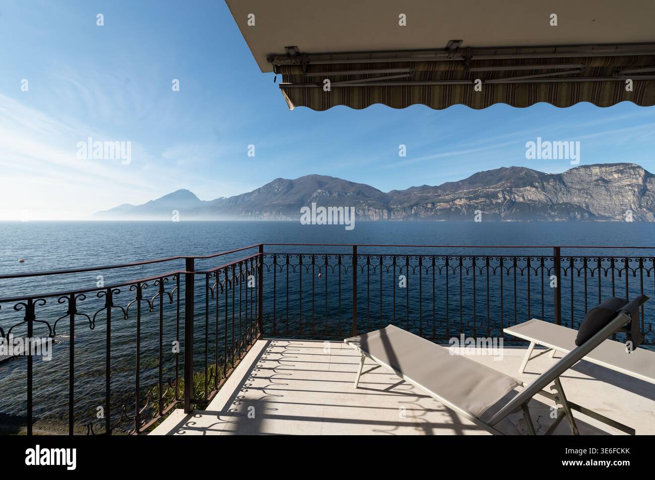 Elegante Luxus-Villa-Terrasse mit Blick auf einen ruhigen italienischen See, mit Liegestühlen, Eisengeländer und Panoramablick auf die Berge, ideal für einen ruhigen Aufenthalt Stockfoto
