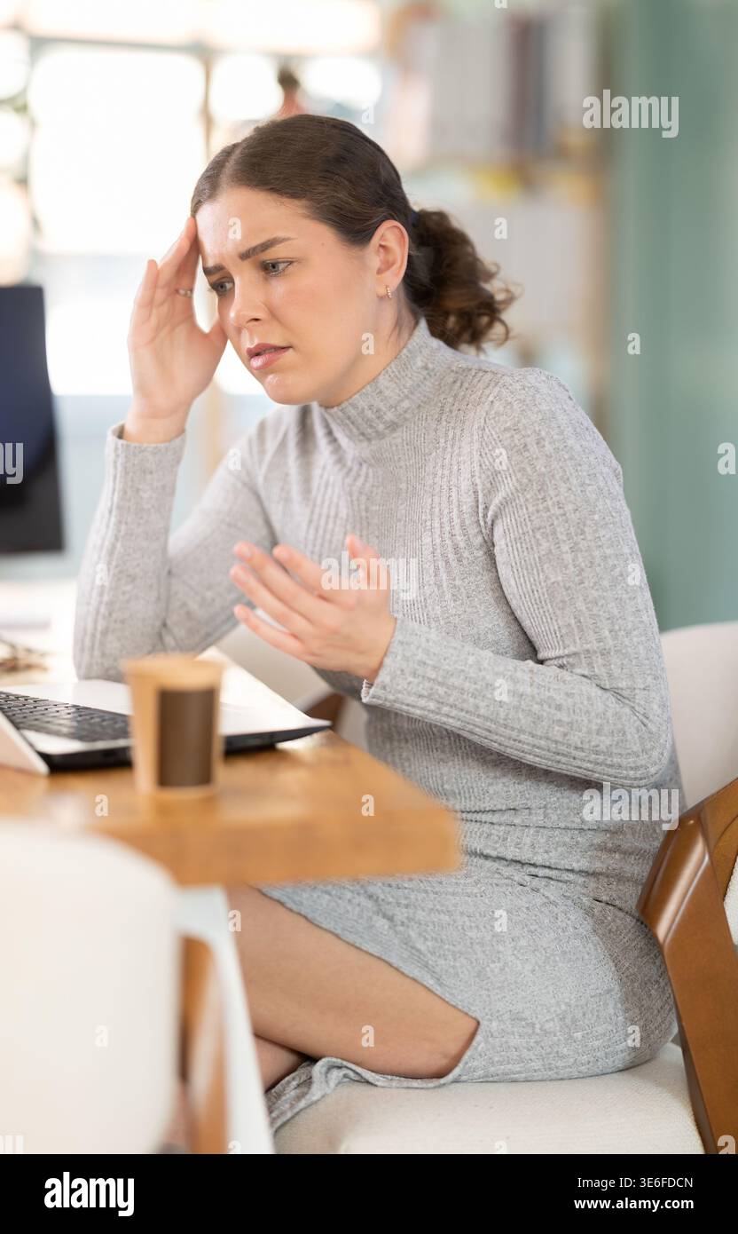 Traurige junge Frau, die im Büro am Laptop arbeitet Stockfoto