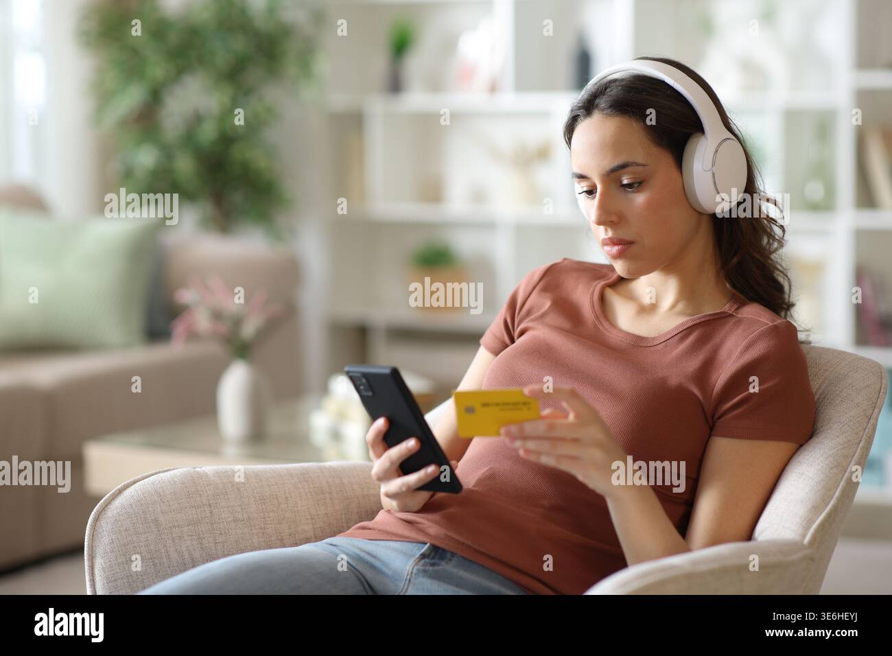 Frau, die Kopfhörer trägt, zahlende Medien online mit Telefon und Kreditkarte zu Hause Stockfoto