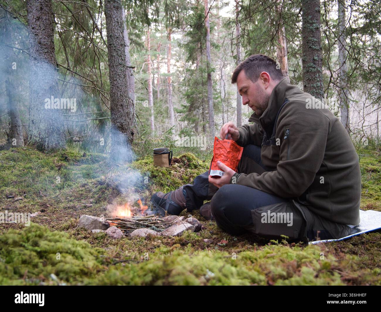 Mann, der Überlebensfutter am Lagerfeuer im Wald in Schweden zubereitet Stockfoto