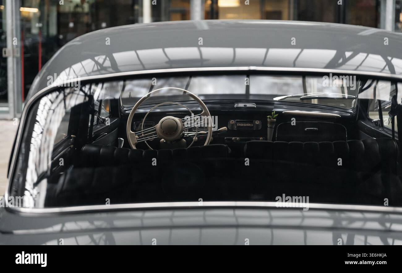 Innenansicht eines Oldtimers durch Heckscheibe. Altes Auto-Interieur mit einem dünnen elfenbeinfarbenen Lenkrad, Retro-Armaturenbrett und schwarzen Ledersitzen. Stockfoto
