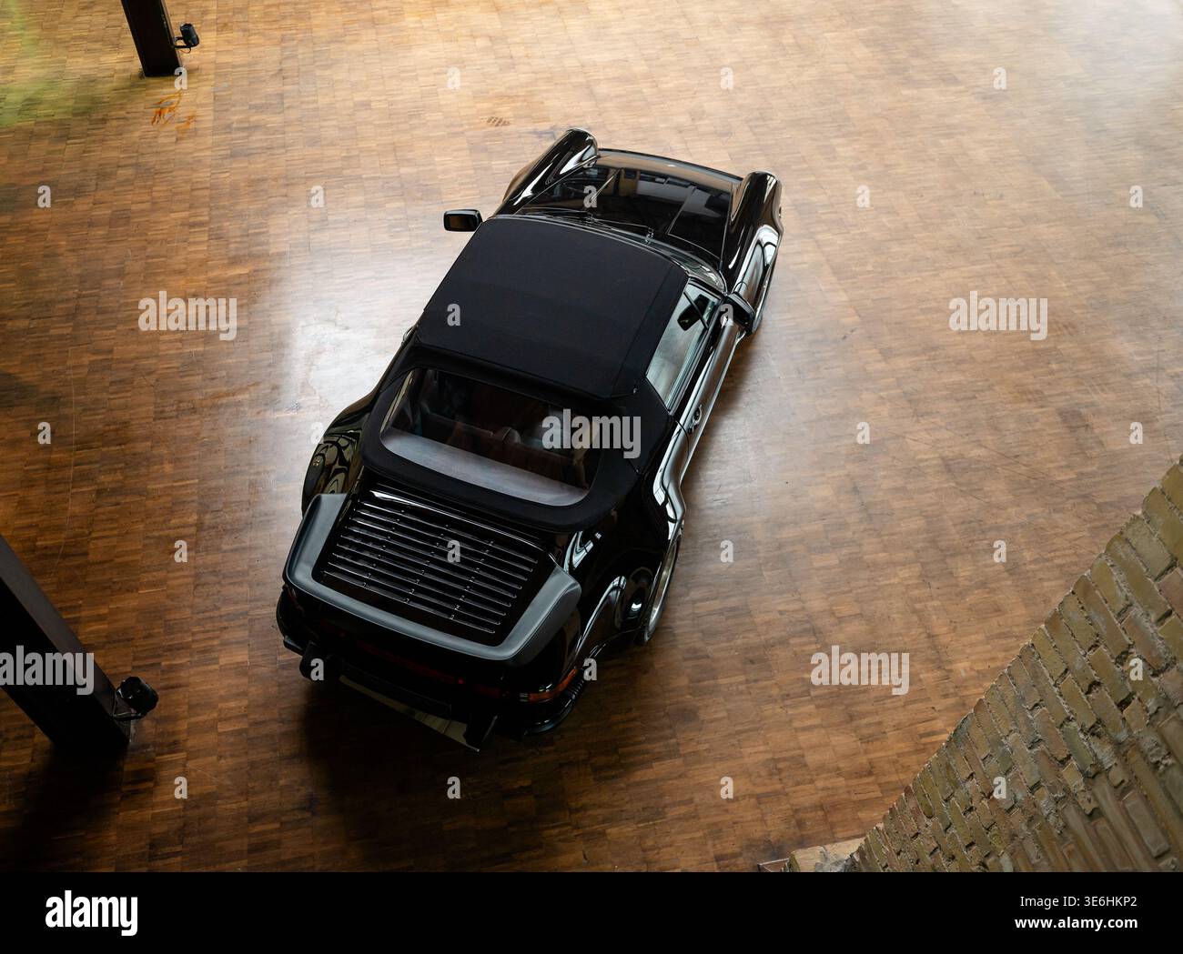 Schwarzes klassisches Porsche 911 Cabriolet auf Parkettboden. Eine Top-down-Perspektive eines schwarzen Porsche 911 Cabriolets aus den 1980er Jahren mit einem Softtop. Stockfoto