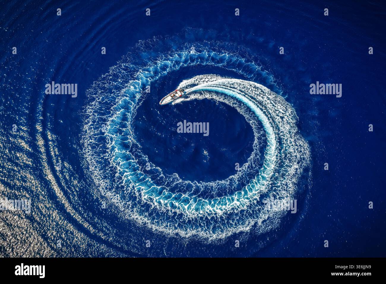 Hohe Sicht von oben auf ein Motorboot, das einen Kreis aus Blasen bildet und mit seinem Motor über dem blauen Ozean surft Stockfoto