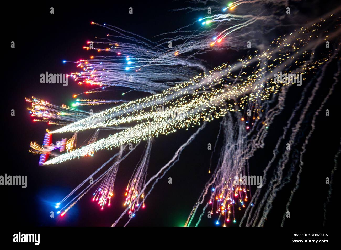 Lebendige Nachtflugshow mit farbenfrohen Feuerwerken, pyrotechnischen Pfaden und beleuchteten Flugzeugen, die über einen dunklen Himmel ziehen und für Aufregung sorgen Stockfoto