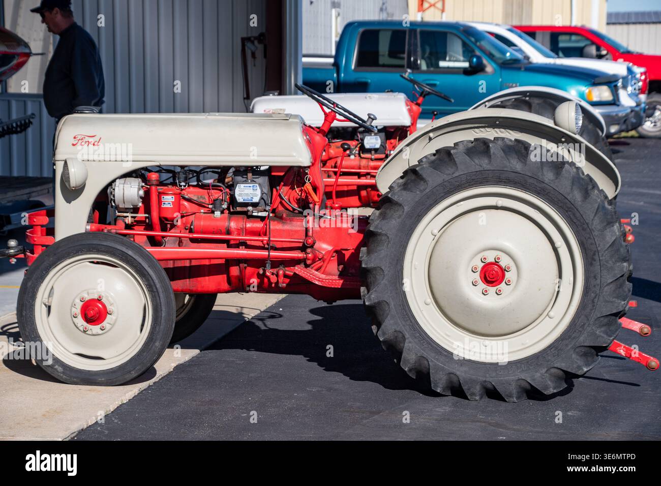 Ford-Traktor in Rot und Creme, der draußen auf einer Messe für Landfahrzeuge geparkt wurde, zeigt klassische Maschinen, große Hinterreifen und freiliegende Motorkomponenten Stockfoto
