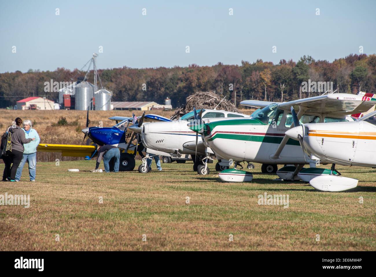 Eine Reihe von kleinen einmotorigen Flugzeugen, die auf einem grasbewachsenen Landflugplatz parkten, mit Piloten und Zuschauern, die im Herbst sprechen und leichte Wartungsarbeiten durchführen Stockfoto