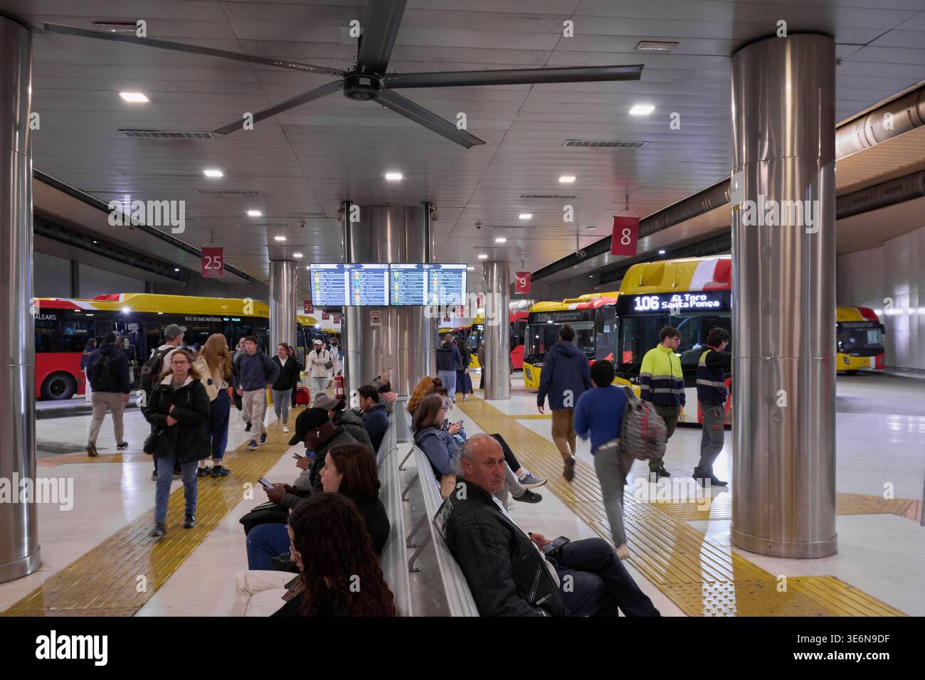 Mallorca. Spanien - 07. April 2026: Pendler sitzen auf Bänken am Bahnhof Palma Intermodal. Ein digitales Abfahrtstafel zeigt die Busfahrpläne oben an Stockfoto