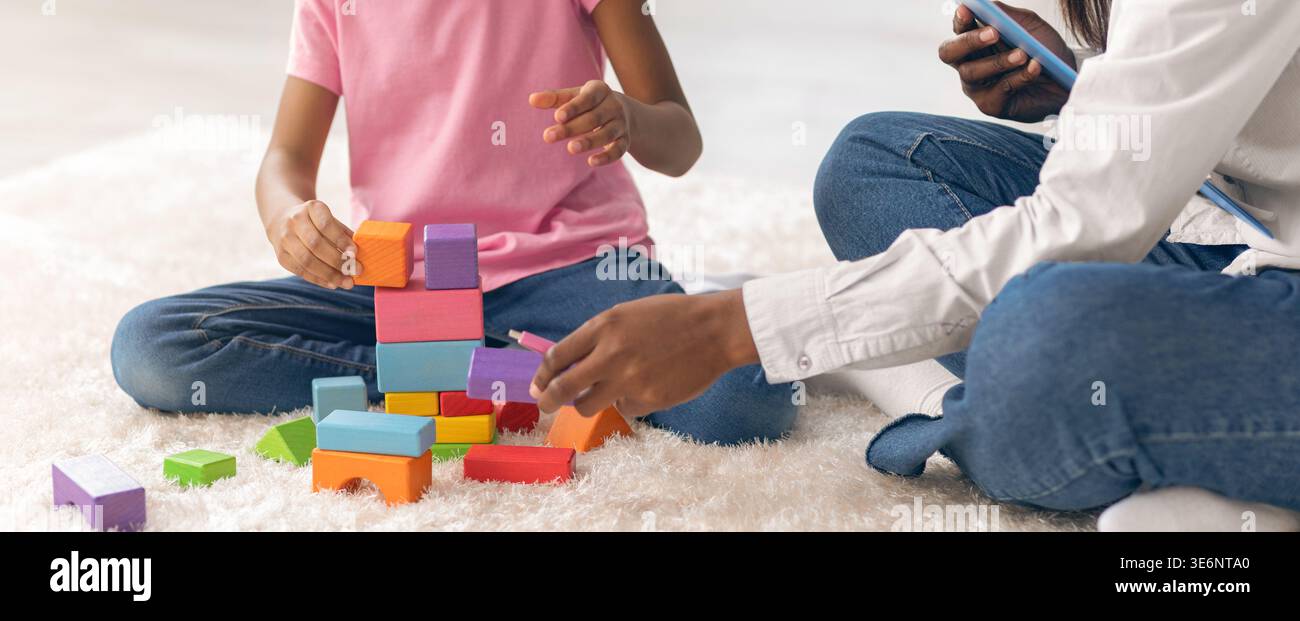 Kinder bauen mit bunten Blöcken auf einem weichen Teppich, während ein Erwachsener mit einem Telefon interagiert Stockfoto