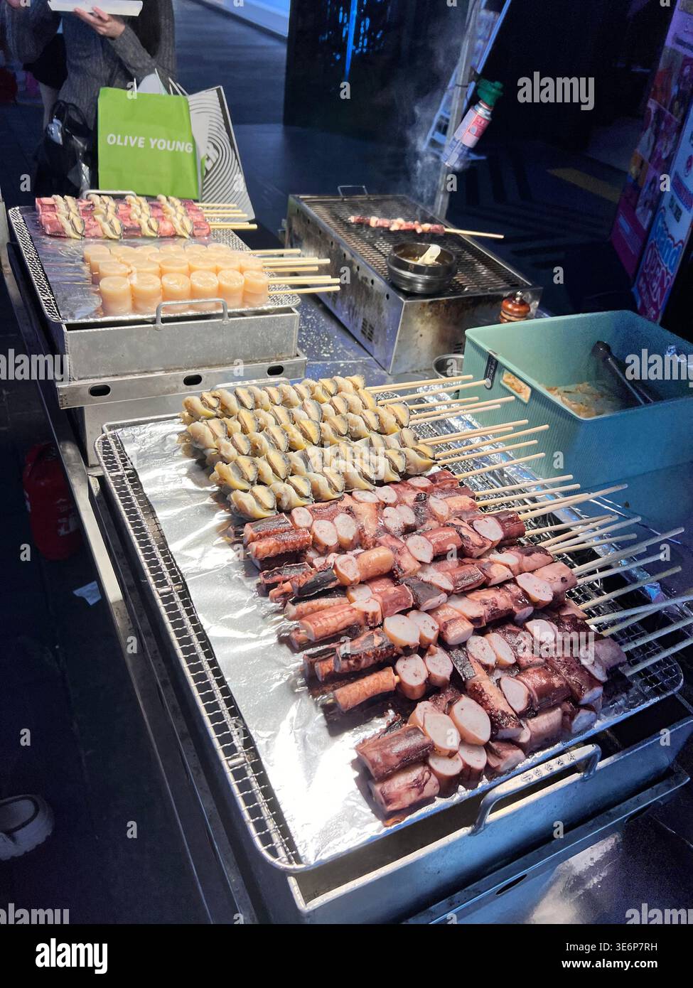 Spieße mit gegrillten Meeresfrüchten auf einem Marktgrill in Myeong-dong, Seoul, Südkorea. - Smartphone-aufgenommenes Stockfoto