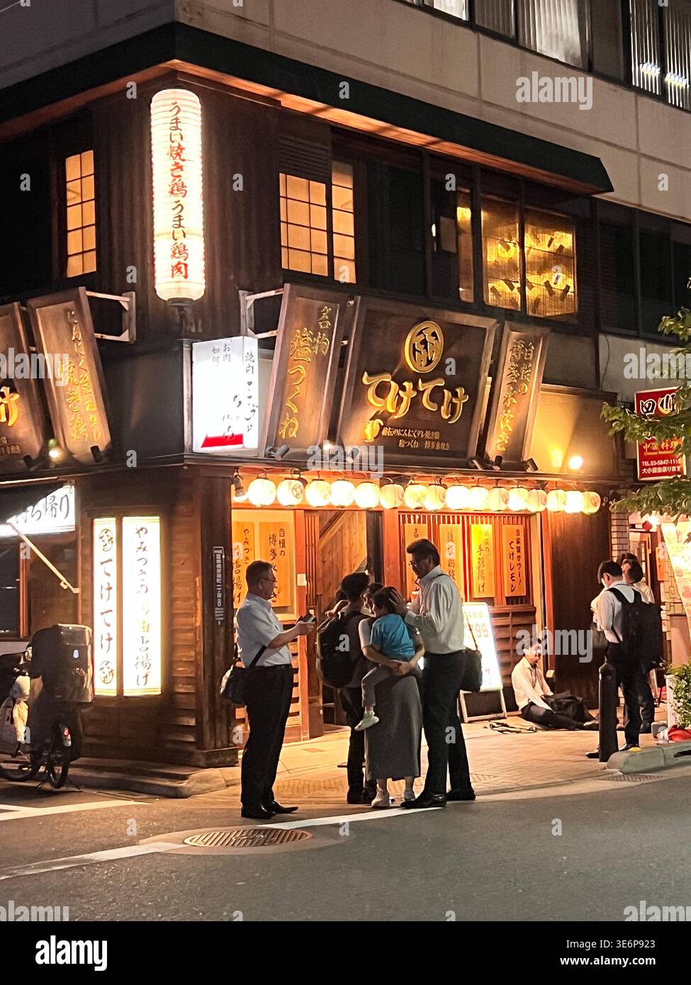 Menschen, die nachts in Tokio, Japan, vor einem beleuchteten Restaurant an einer Straßenecke stehen. Stockfoto