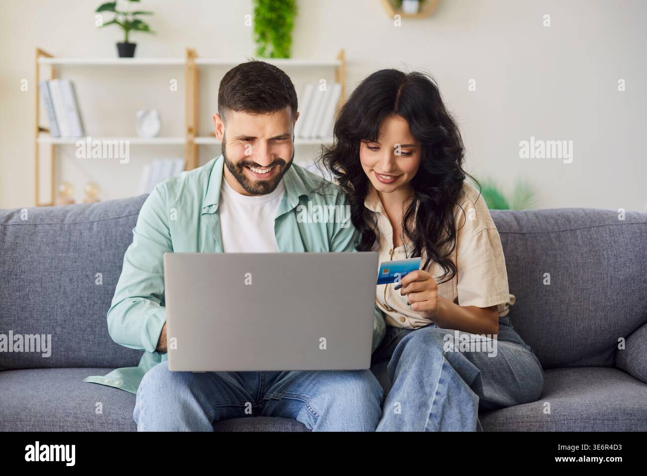 Glückliches Paar zahlt online mit Bankkarte zu Hause auf dem Sofa, mit einem Laptop zusammen Stockfoto