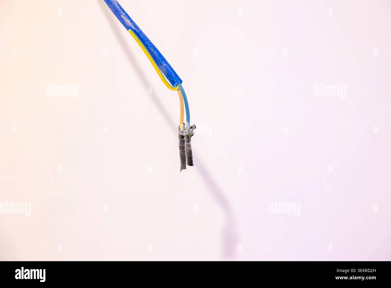 Freiliegende Elektrodrähte, die in unfertigen Innenräumen von der Decke hängen, beschädigte Isolierung. Konzept: Elektrische Gefahr Stockfoto