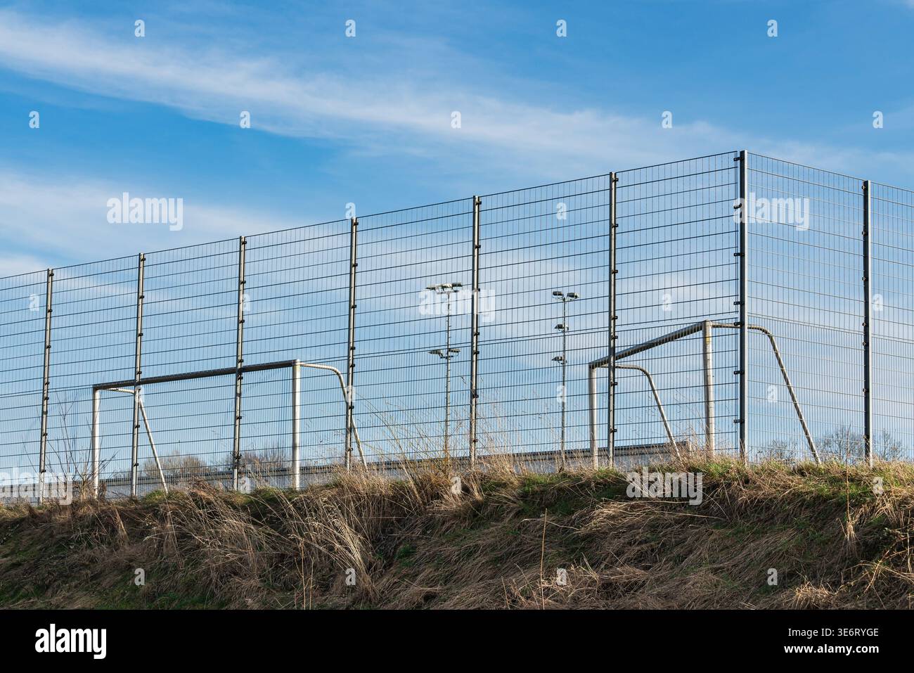 Zwei Fußballtore sitzen auf einem grasbewachsenen Gelände in der Nähe eines hohen Zauns. Der Zaun umgibt das Feld. Der Himmel ist klar und blau. Es sind keine Spieler in Sicht auf Th Stockfoto