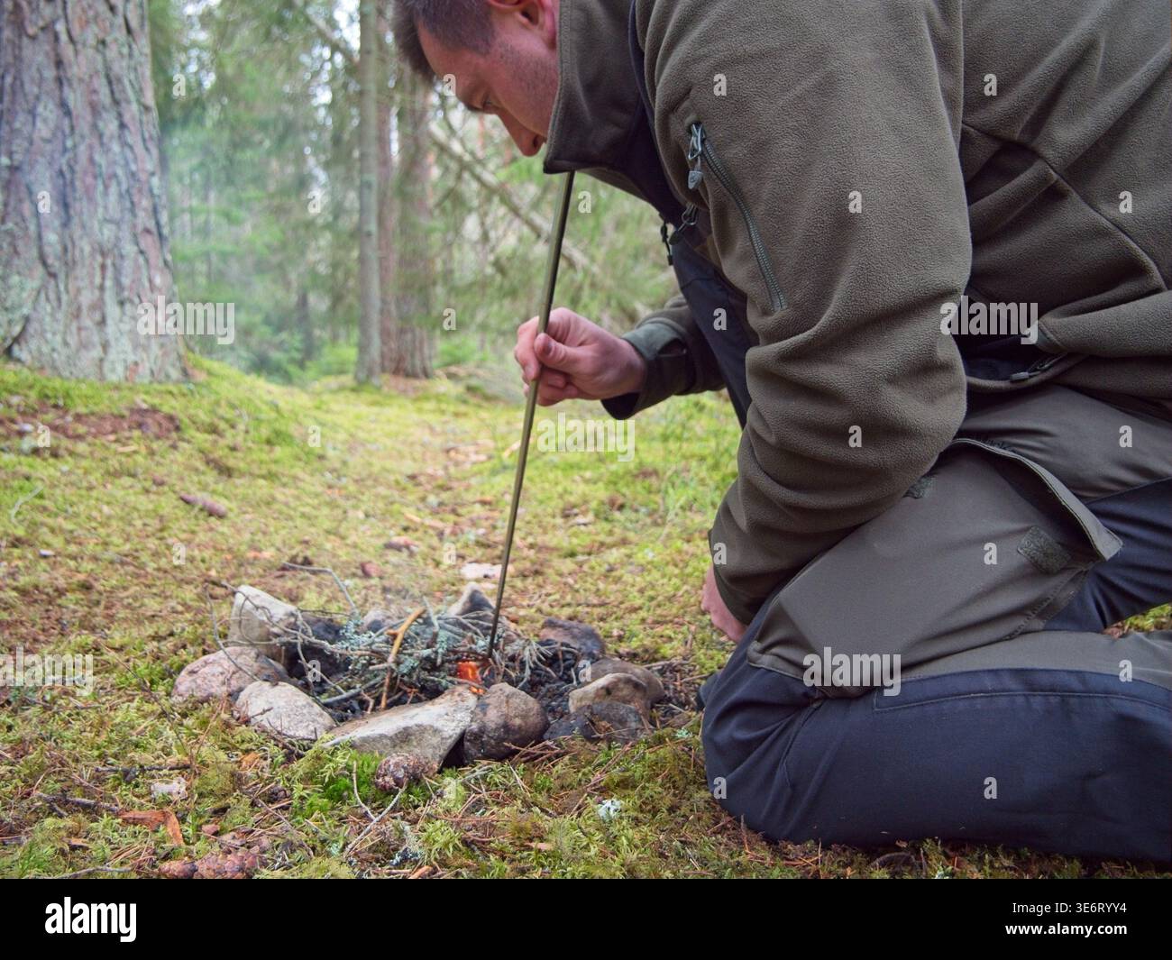 Mann, der ein kleines Lagerfeuer mit Stock während des Bushcraft-Campings pflegt Stockfoto
