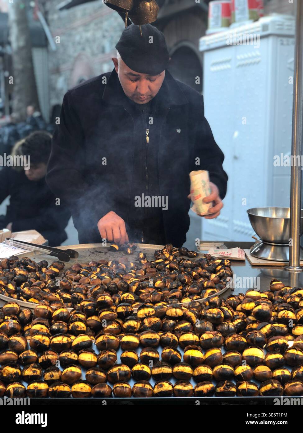 Straßenverkäufer, der im Winter tagsüber im Freien geröstete Kastanien mit traditioneller Street Food-Atmosphäre verkauft. - Smartphone-aufgenommenes Stockfoto
