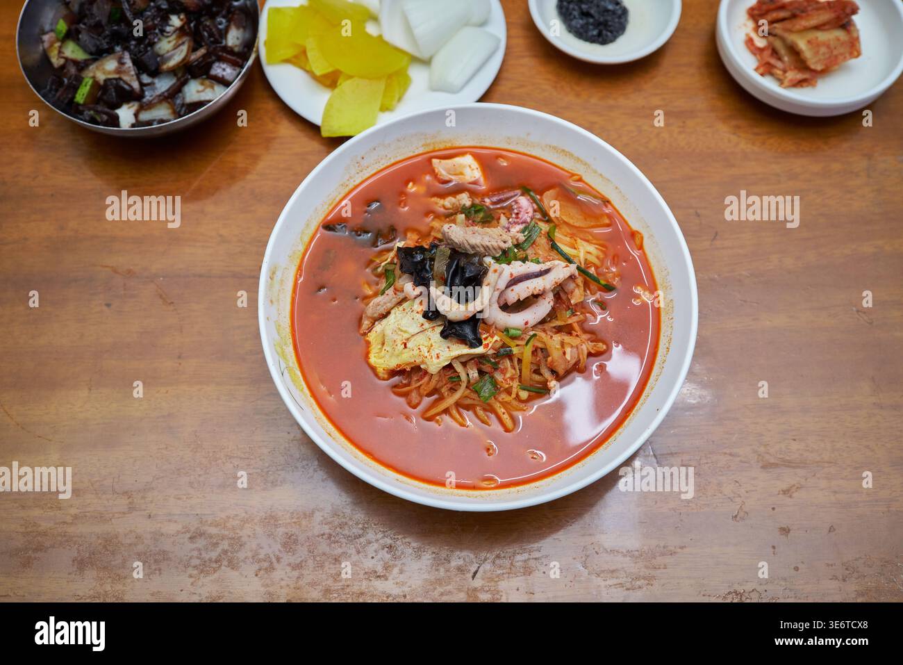 Verschiedene Schüsseln Jjamppong, Koreas geliebte scharfe Nudelsuppe. Fängt die feurige rote Brühe mit frischen Meeresfrüchten, Schweinefleisch und lebendigem Gemüse ein. Stockfoto