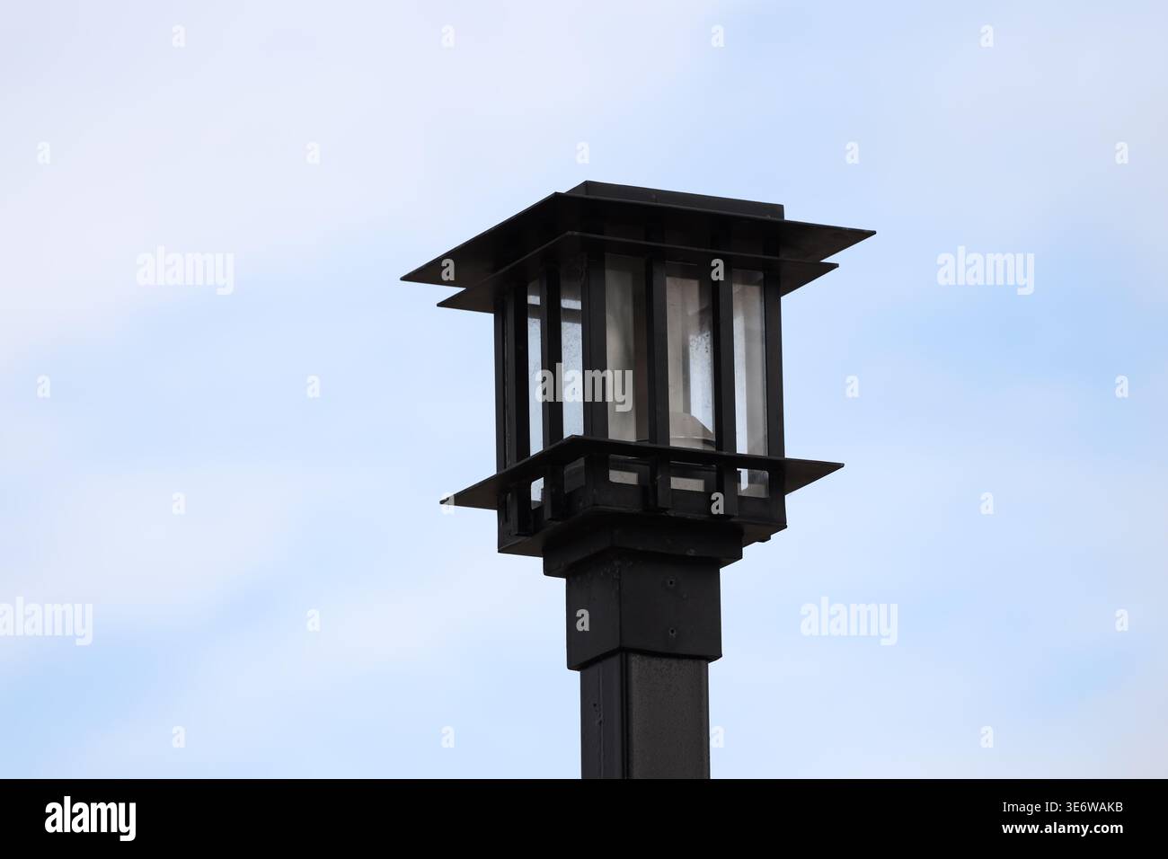 Leuchte aus schwarzem Schmiedeeisen (Licht) am Pol gegen blaugrauem Himmel (Makro, Nahaufnahme) Stockfoto
