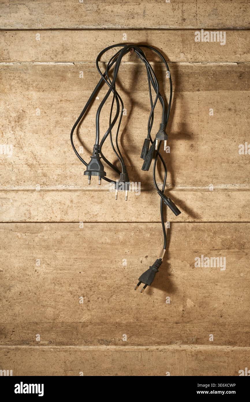 Hängende schwarze Stromkabel und Stecker an einer Wand aus schmutzigem, strukturiertem Holz mit Kopierraum, Konzept für Kabelgewirr und Organisation Stockfoto