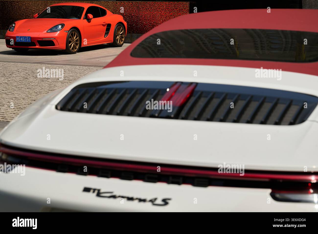 Heckdeckeldeckel und rotes Verdeck eines weißen Porsche 911 Carrera 4S mit orangefarbenem Porsche 718 im Hintergrund, Shanghai, China, Asien. Stockfoto