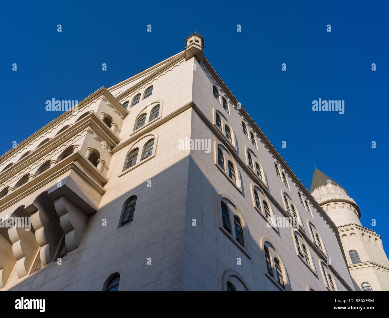 Abstrakte Perspektive mit niedrigem Winkel, Blick auf die Ecke eines weißen Schlossgebäudes mit kunstvollen Balkonen und einem weit entfernten Turm gegen einen klaren Turm Stockfoto