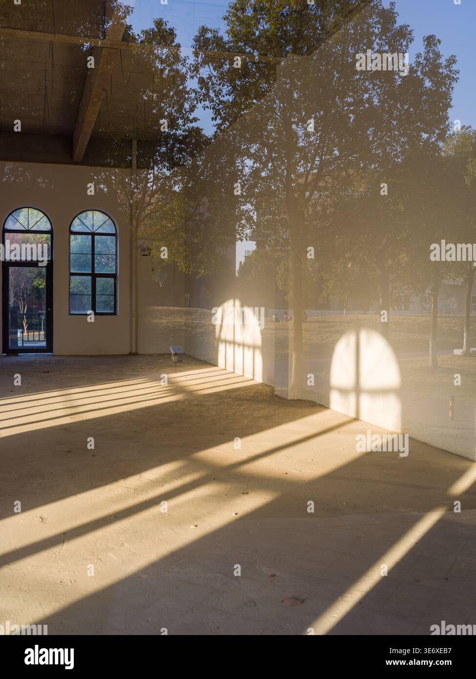 Vertikale Perspektive eines leeren, überdachten Korridors, in dem helles Sonnenlicht dramatische bogenförmige Fensterschatten und lineare Muster über den gesamten Außenbereich wirft Stockfoto