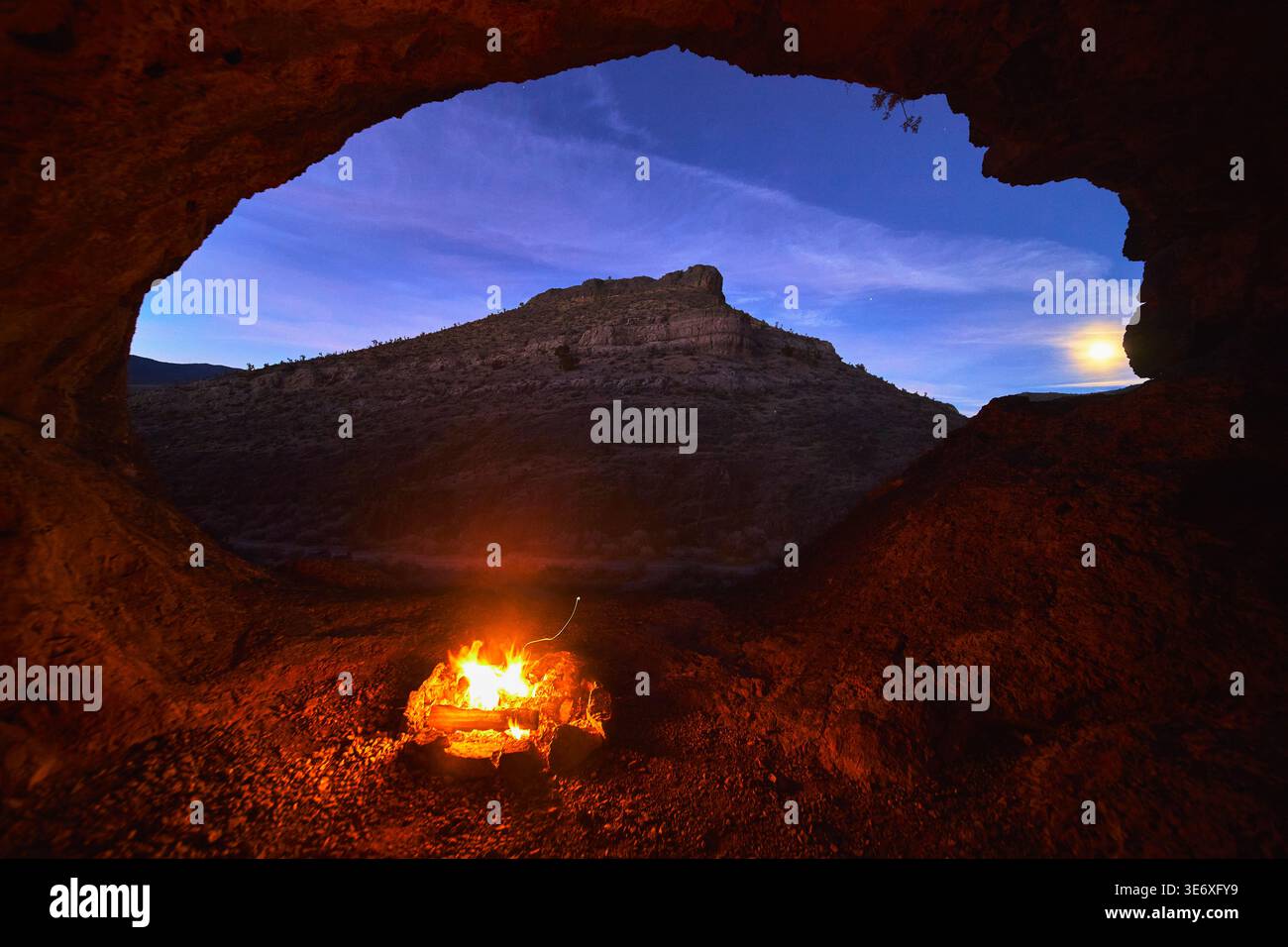 Lagerfeuer in der Wüstenhöhle, die den Blue Hour Mountain und den Mondschein umrahmt Stockfoto