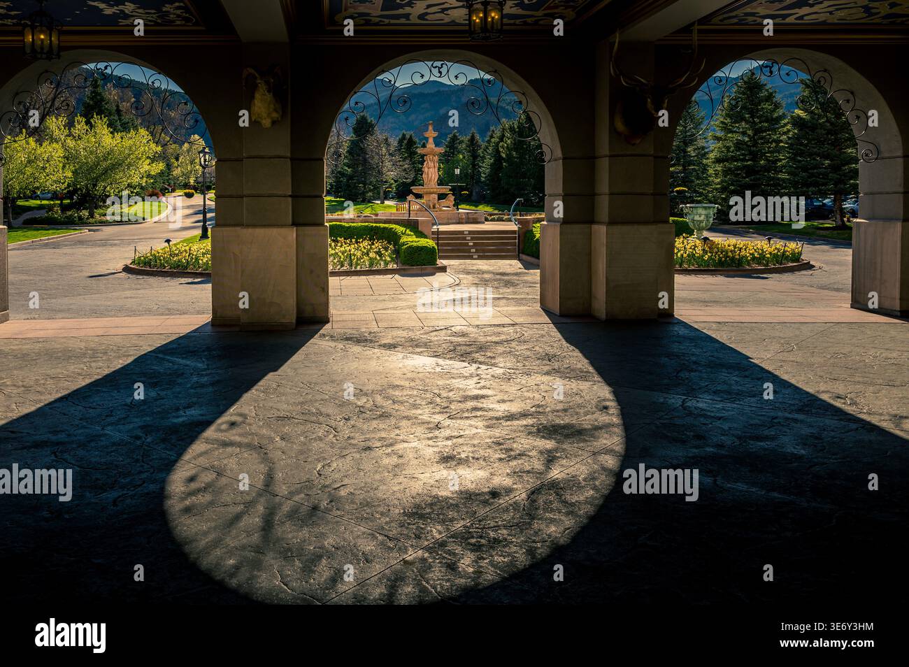 Sonnendurchflutete Steinbögen, die den Bergbrunnen und den Gartenhof mit dramatischen Schatten umrahmen Stockfoto