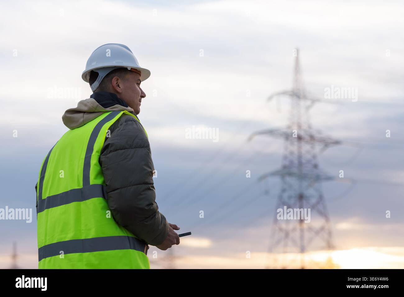 Junge männliche Elektroingenieure überprüfen Hochspannungsleitungen mit einem Laptop in einem Außenbereich während der Sonnenuntergänge. Stockfoto
