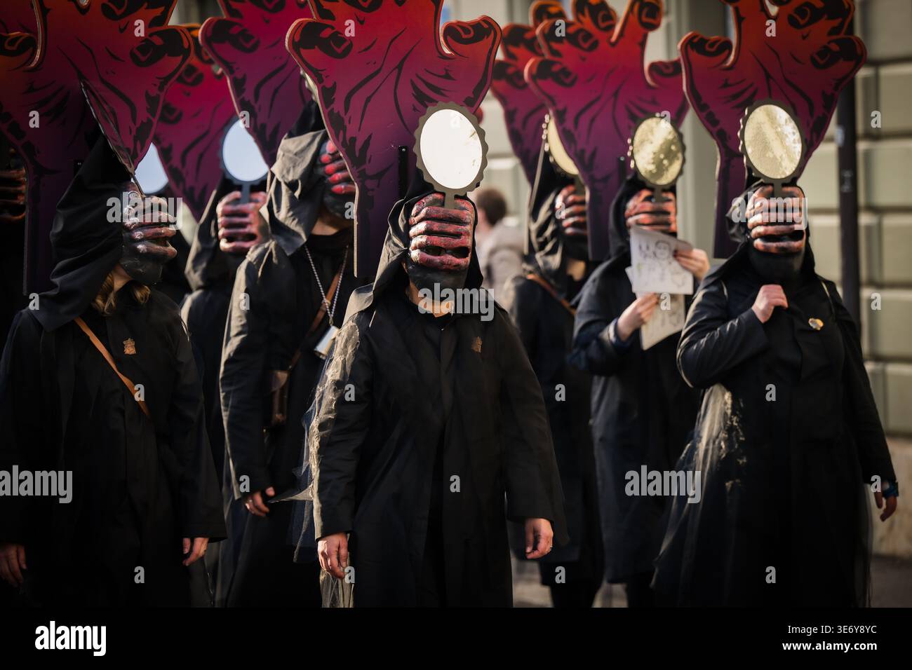 Basel, Schweiz - 10. März 2025: Blick auf Kapuzenfiguren mit Masken und Spiegeln, die bei der Fasnacht-Parade marschieren, ein Schwarzes Meer gegen den gedämpften ci Stockfoto