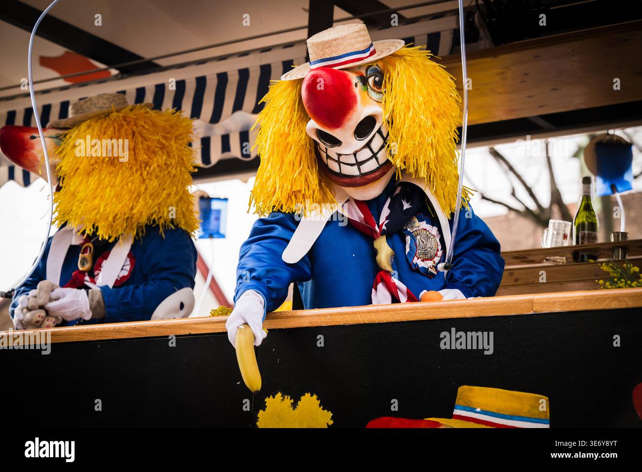 Basel, Schweiz - 10. März 2025: Blick auf eine pulsierende Fasnacht-Parade, bei der maskierte Figuren in blauen Kostümen und gelben Perücken Bananen anbieten Stockfoto