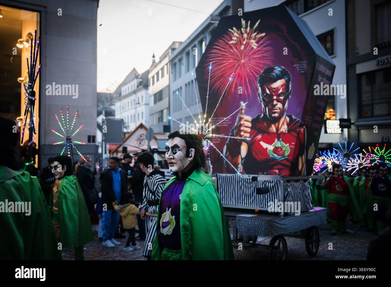 Basel, Schweiz - 10. März 2025: Blick auf kostümierte Figuren ziehen während der Fasnacht durch die Straßen der Stadt, deren leuchtende grüne Umhänge sich von ag abheben Stockfoto