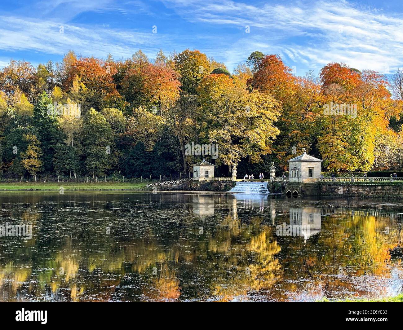 Herbstbäume spiegeln sich in einem ruhigen See mit farbenfrohen Laub und kleinen Pavillongebäuden in einem britischen Park - Smartphone-aufgenommenes Stockfoto