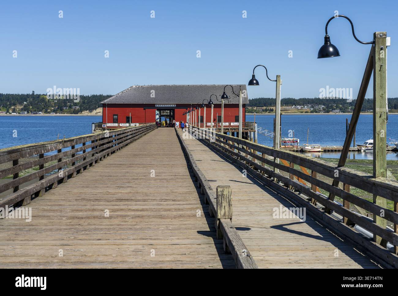 Breiter hölzerner Pier, der zum roten Gebäude der Coupeville Wharf von 1909 in Penn Cove Whidbey Island führt Stockfoto