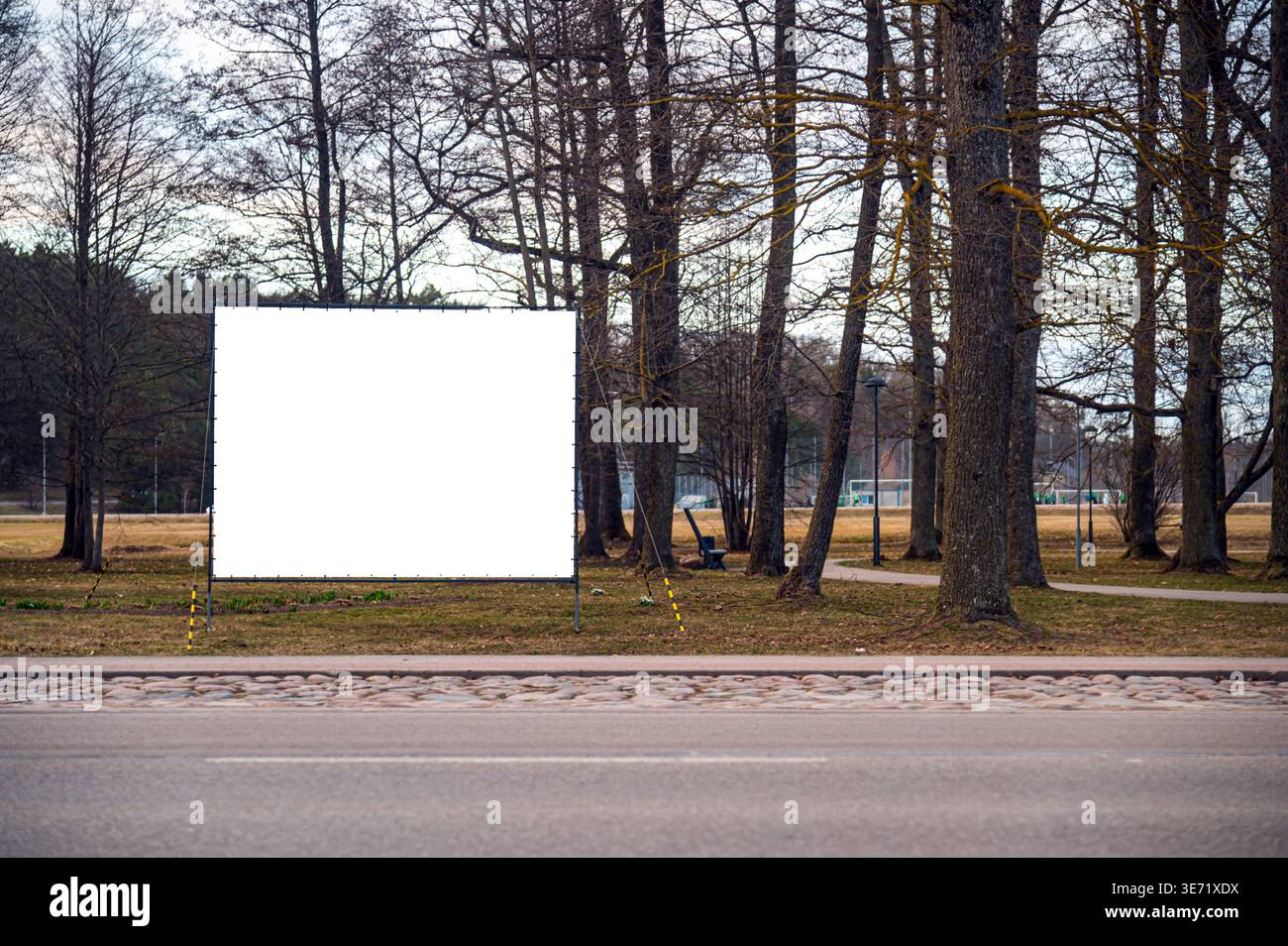 Eine leere Vorlage steht an einem sonnigen Tag zwischen Bäumen in einem Park neben einer Straße. Stockfoto