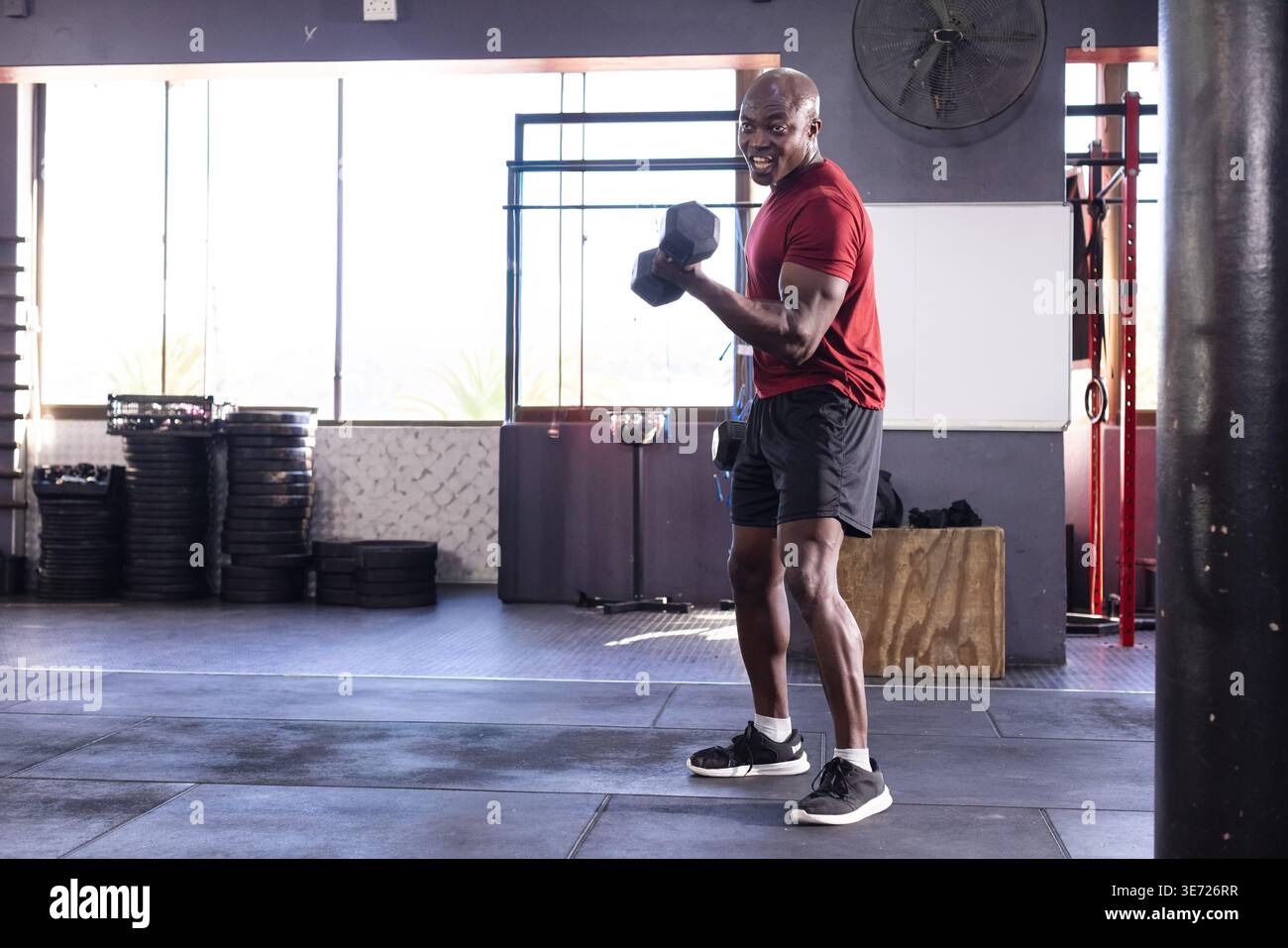 Afroamerikaner mit Hexenhantel, Bizepscurl im Fitnessstudio in der Nähe von Tellern, Kopierraum. Athlet, Gewichte, Training, Kraft, Sonnenlicht, einstauben Stockfoto