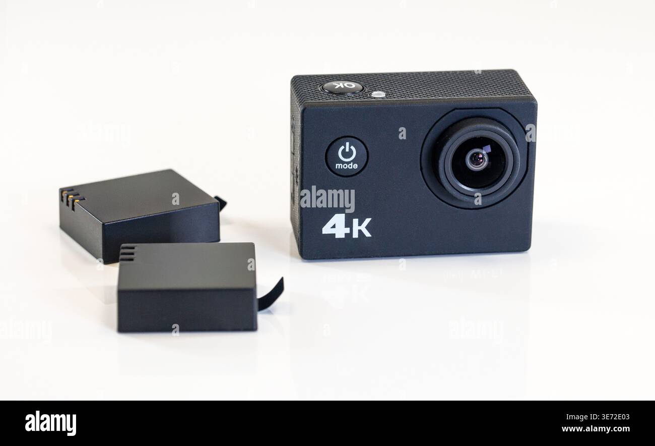Schwarze 4K Action-Kamera mit zwei Batterien auf reflektierendem weißem Hintergrund, bereit für extreme Aufnahmen Stockfoto