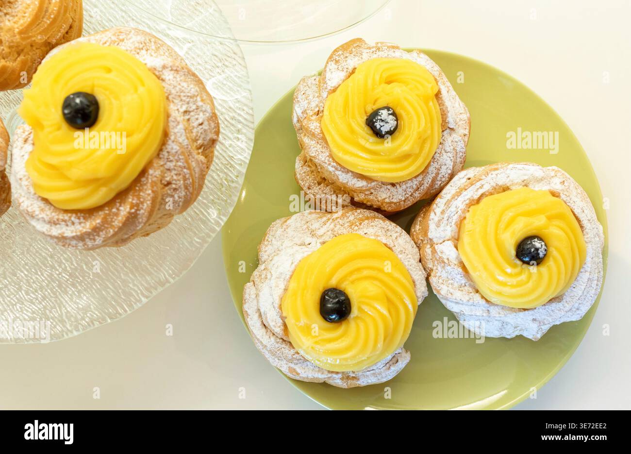 Zeppole di San Giuseppe, traditionelles italienisches Choux-Gebäck mit weichem Ring, einem Schuss Vanillecreme und einer dunklen schwarzen Kirsche auf der Oberseite, die mit Puderzucker für die Feier des St. Josephs-Tages bestäubt ist Stockfoto