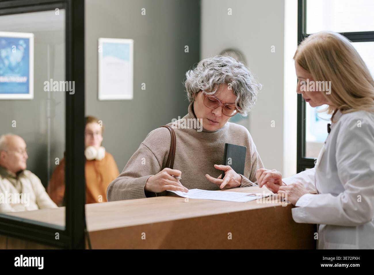 Frau, die medizinische Formulare an der Rezeption der Klinik unterschreibt Stockfoto
