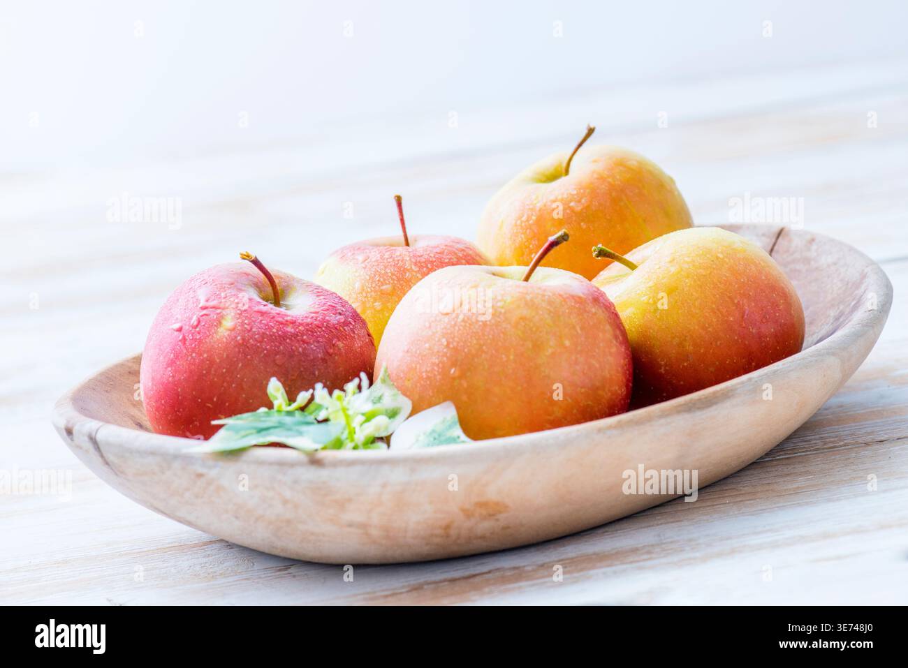 Frisch geerntete rote und gelbe Äpfel mit Wassertropfen auf einem hellen Holztisch Stockfoto