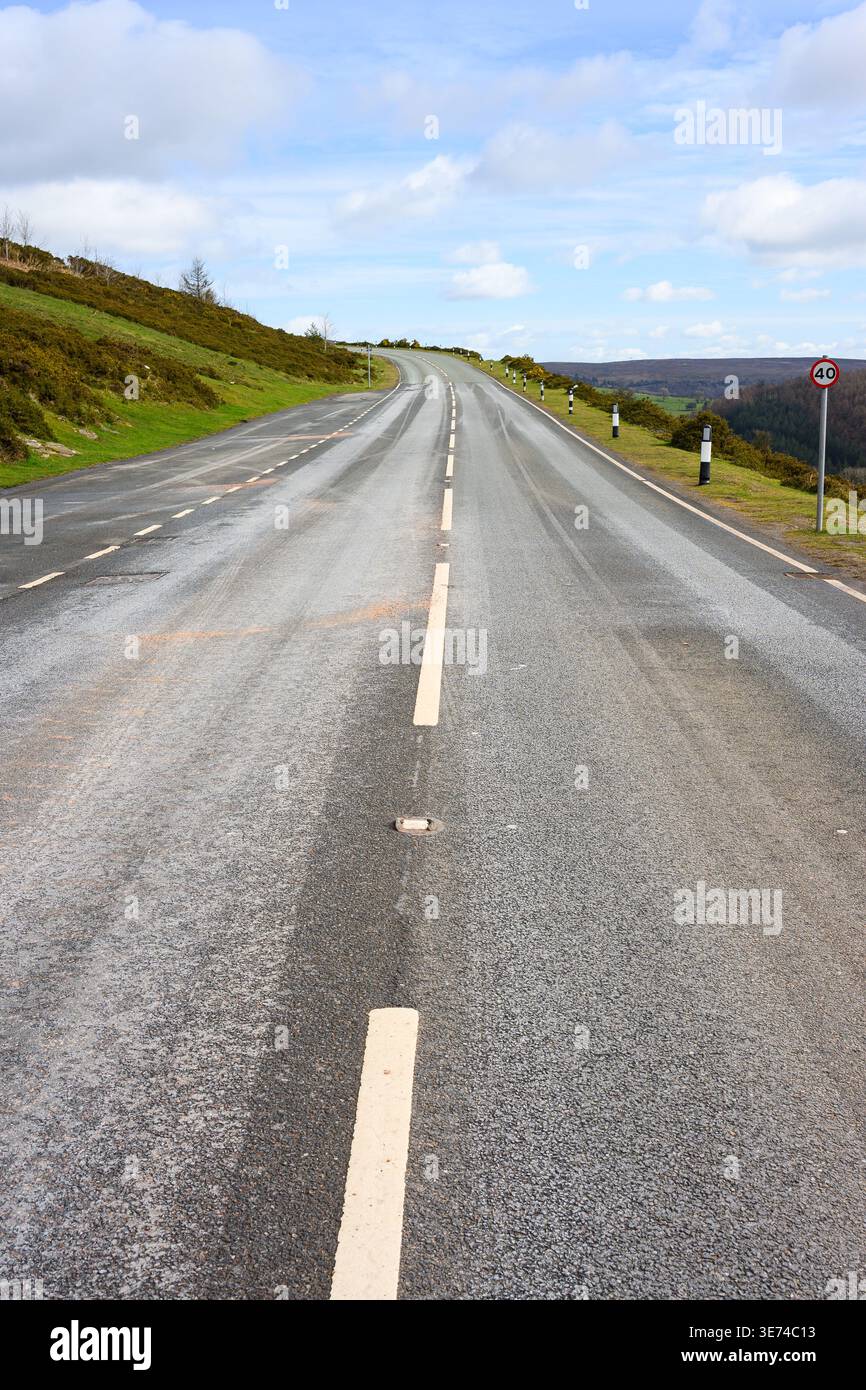 Zweispurige Straße mit Straßenmarkierungen, die bis zum Horizont mit hellem Himmel in Wales ragen Stockfoto