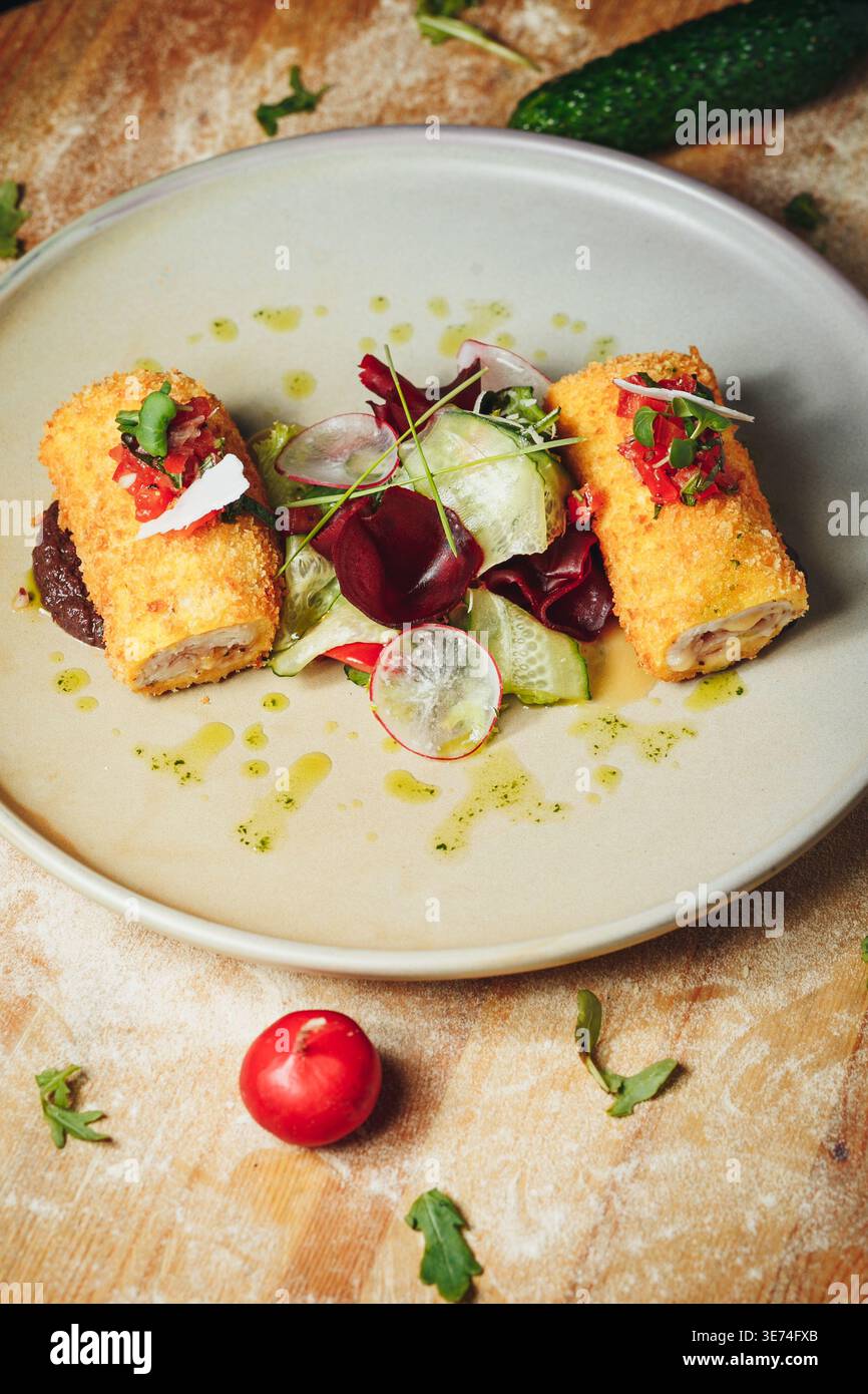Gourmet panierte Hähnchenbrötchen, serviert mit einem frischen Salat aus Rettich-Gurke und Rüben-Scheiben garniert mit Kräuteröl auf einer Keramikplatte. Stockfoto