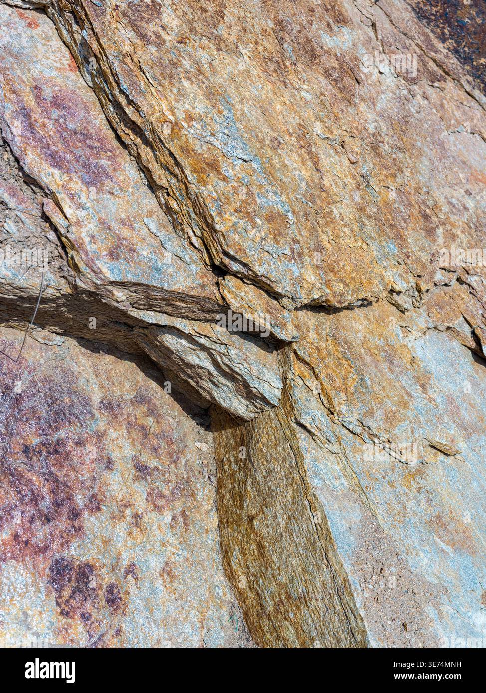 Detaillierte Nahaufnahme einer robusten Felswände mit markantem diagonalem Riss und variierenden Texturen mit Rostflecken und gräulich-blauen Mineralien. Th Stockfoto