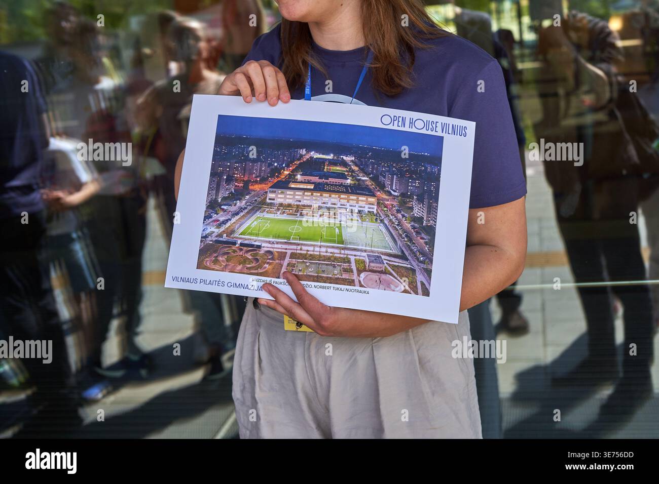Eine Frau, die ein marineblaues T-Shirt und hellfarbene Hose trägt, hält während eines Tag der offenen Tür ein großes Plakat mit einer architektonischen Darstellung Stockfoto
