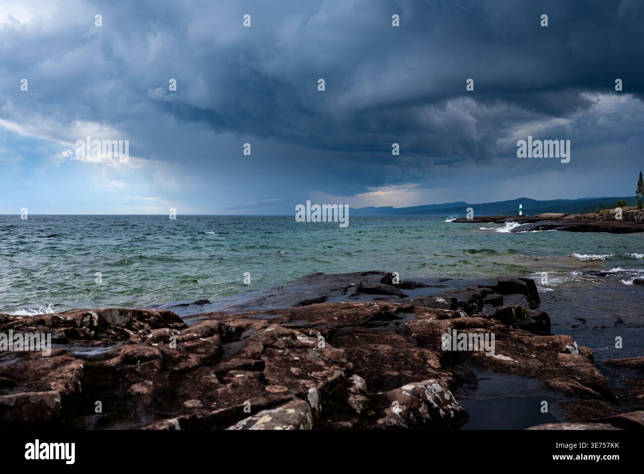 Dramatische Sturmwolken über Rocky Shoreline mit entferntem Leuchtturm und abgehacktem Wasser Stockfoto
