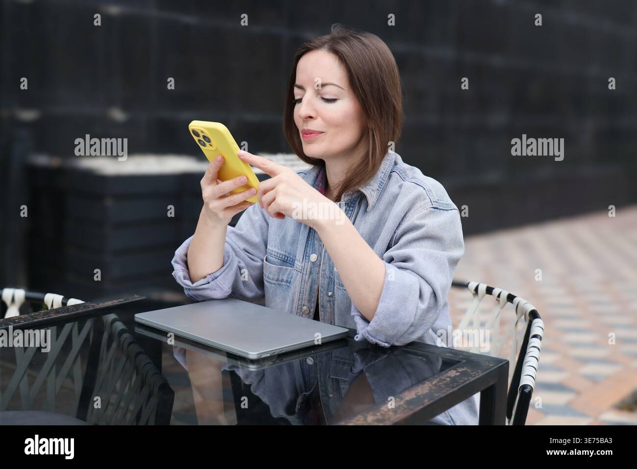 Junge Frau mit Smartphone im Freien. Porträt einer kaukasierin mit Telefon auf der Terrasse des Cafés. Stockfoto