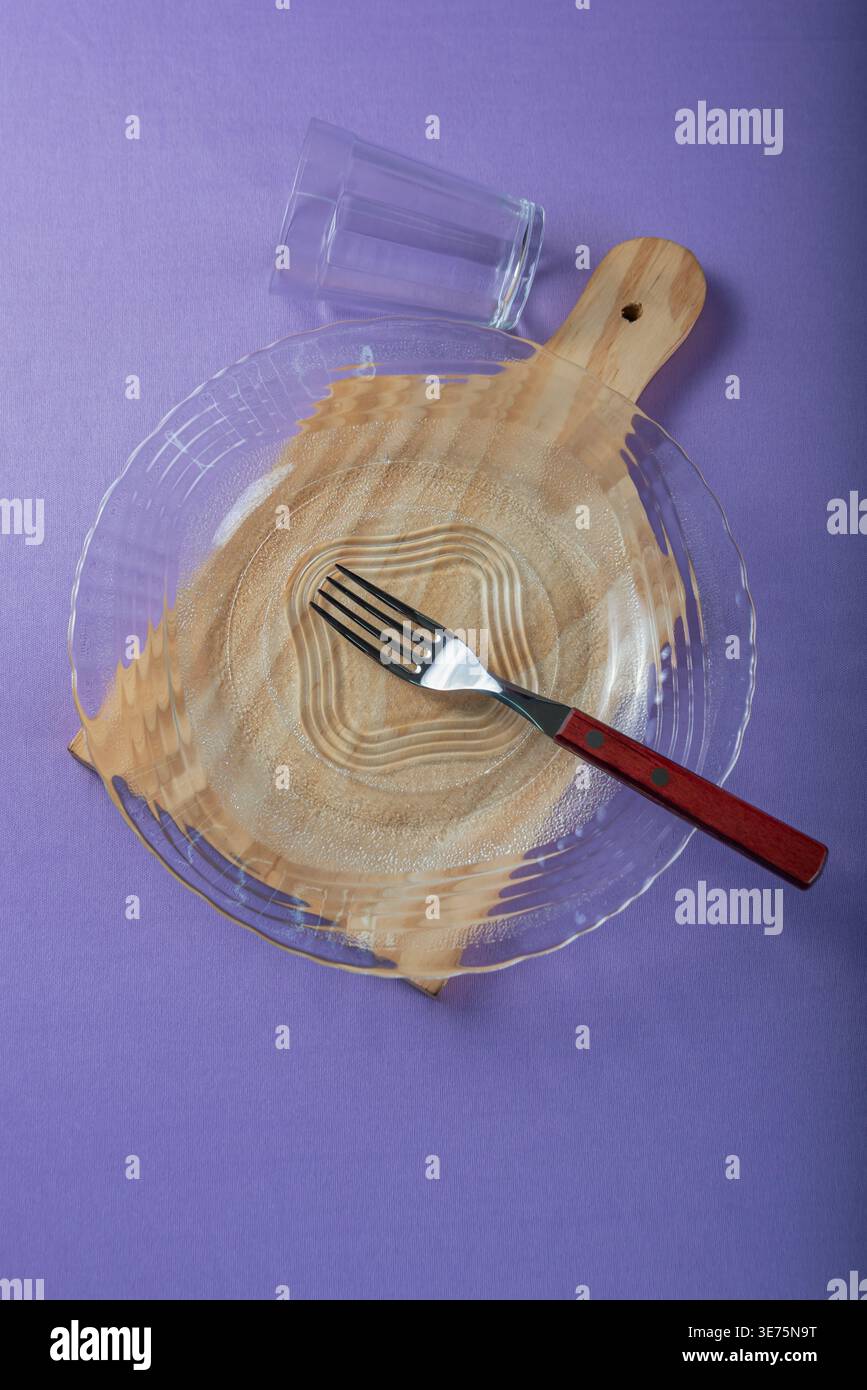 Das Studio-Bild über der Decke zeigt Teller, Holzbrett, Glas und Gabel vor violettem Hintergrund. Sanfte Beleuchtung, klare Texturen und Erdtöne sorgen für ein gesundes Bild Stockfoto